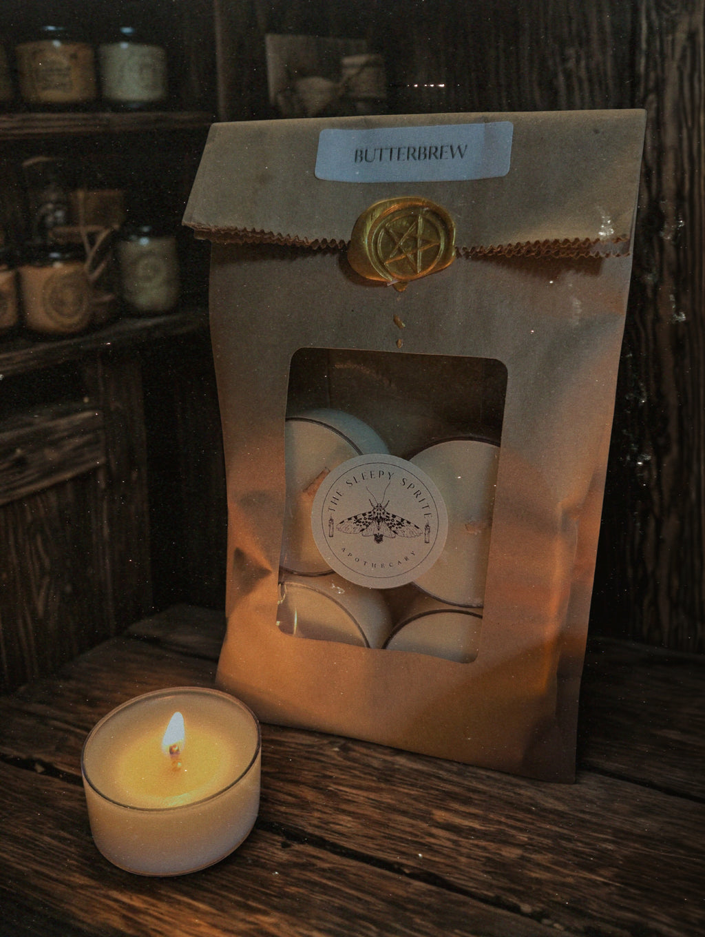 Packaged tealight candles with a lit candle on a wooden surface, featuring 'Butterbrew' branding. From the Sleepy Sprite Apothecary. Witchy dark cottagecore aesthetic.
