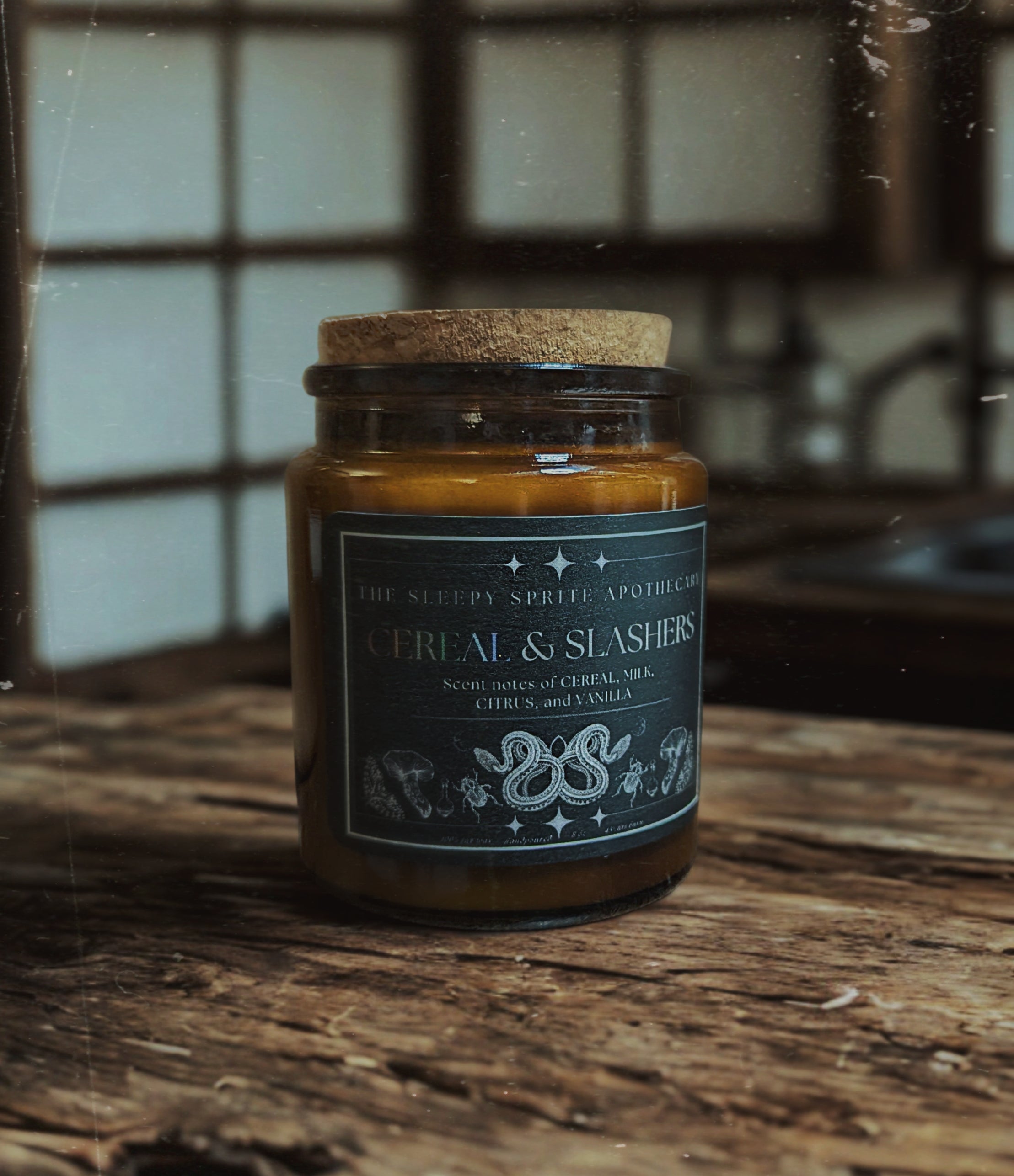 Candle in a glass jar with a cork lid on a wooden surface, featuring a label. From the Sleepy Sprite Apothecary. Fruit loops scented candle.