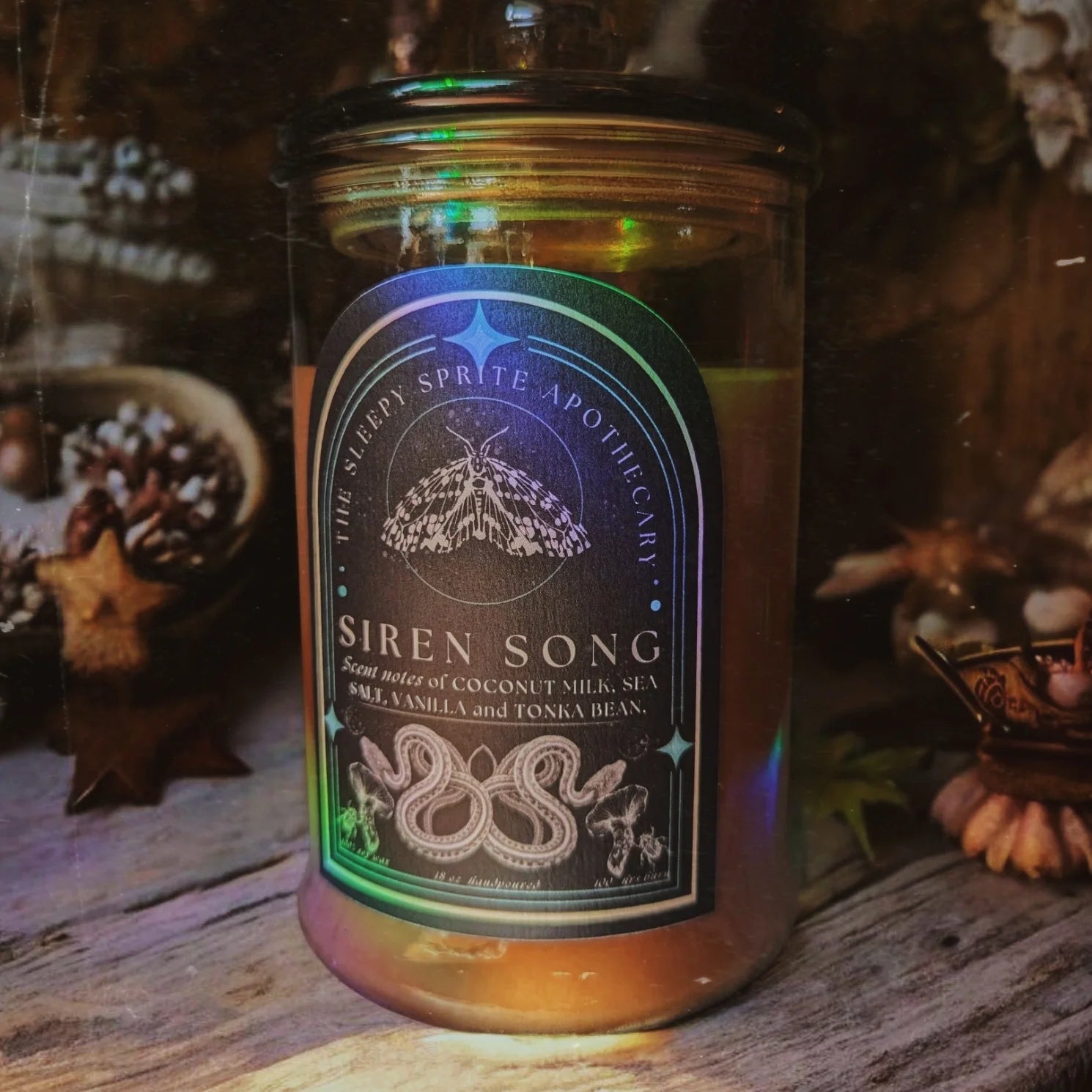 Candle labeled 'Siren Song' with decorative background from The Sleepy Sprite Apothecary. Witchy dark cottagecore aesthetic.