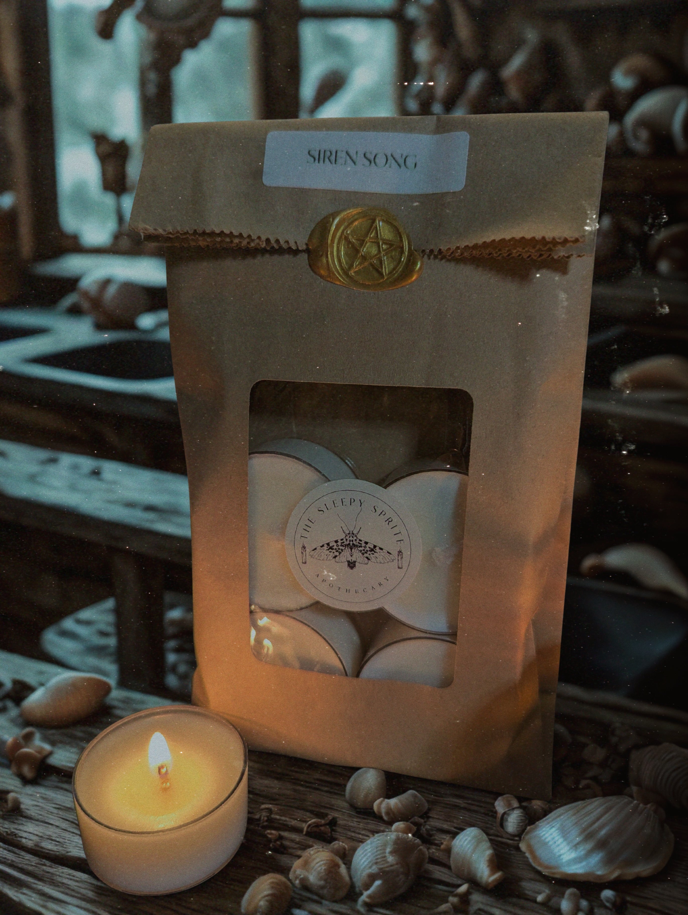 Packaged Tealight candles labeled 'Siren Song' with a lit candle and seashells on a wooden surface. Witchy dark cottagecore aesthetic.