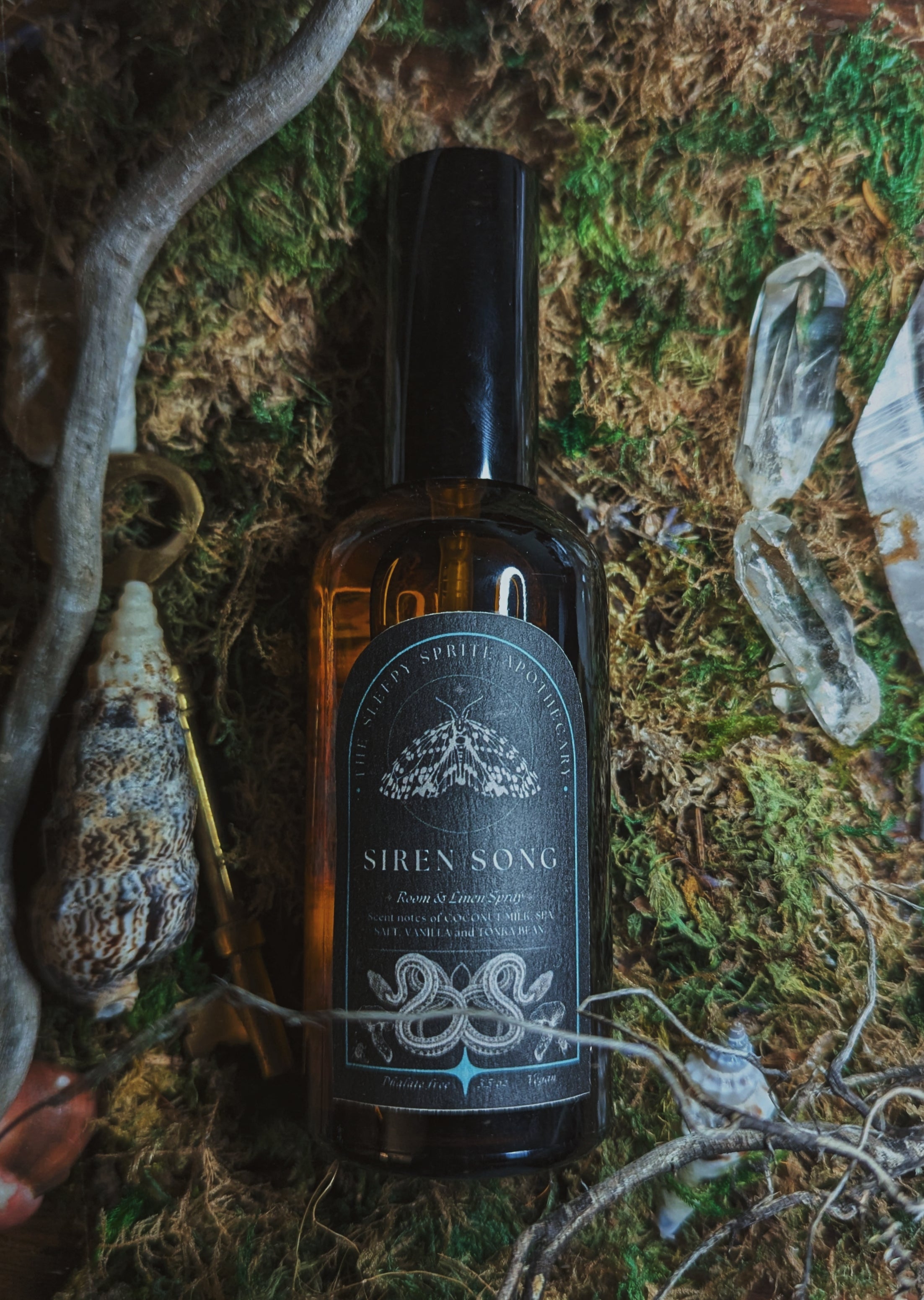Bottle of 'Siren Song' room and linen spray on a textured surface with natural elements. Witchy dark cottagecore aesthetic.