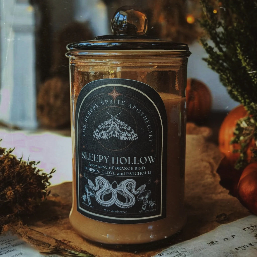 Sleepy Hollow Candle in a glass jar with a decorative label on a rustic background from The Sleepy Sprite Apothecary. Witchy dark cottagecore aesthetic.