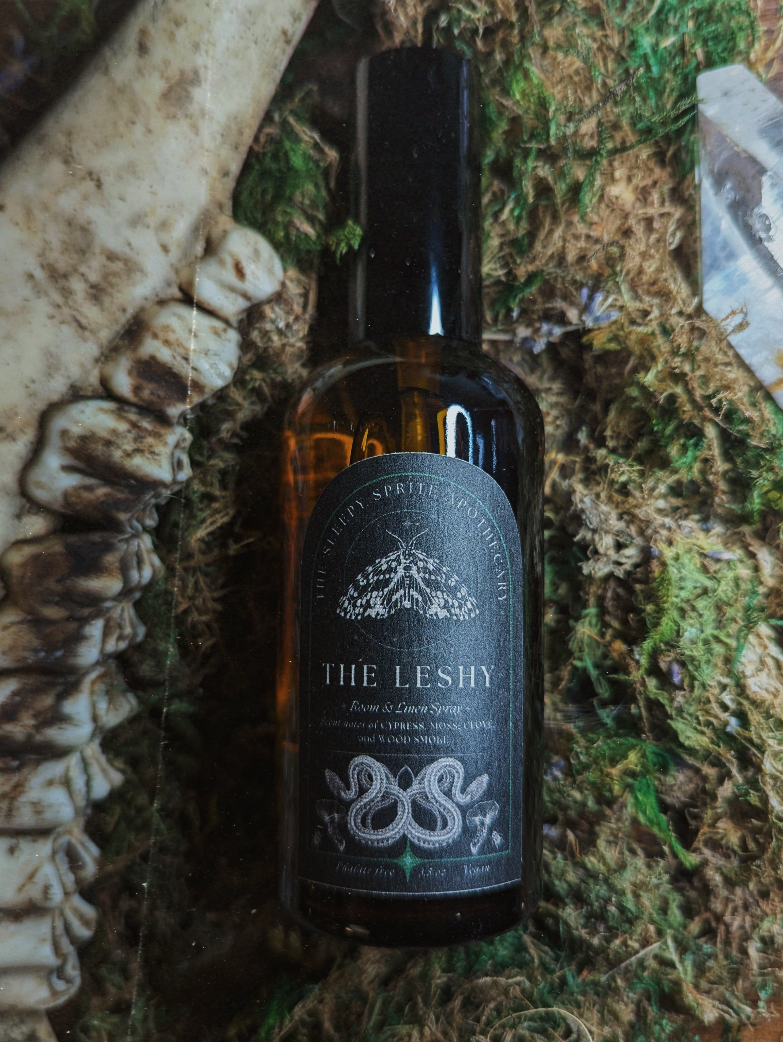Bottle of 'The Leshy'  room and linen spray with a label featuring a moth design on a natural background. Witchy dark cottagecore aesthetic.