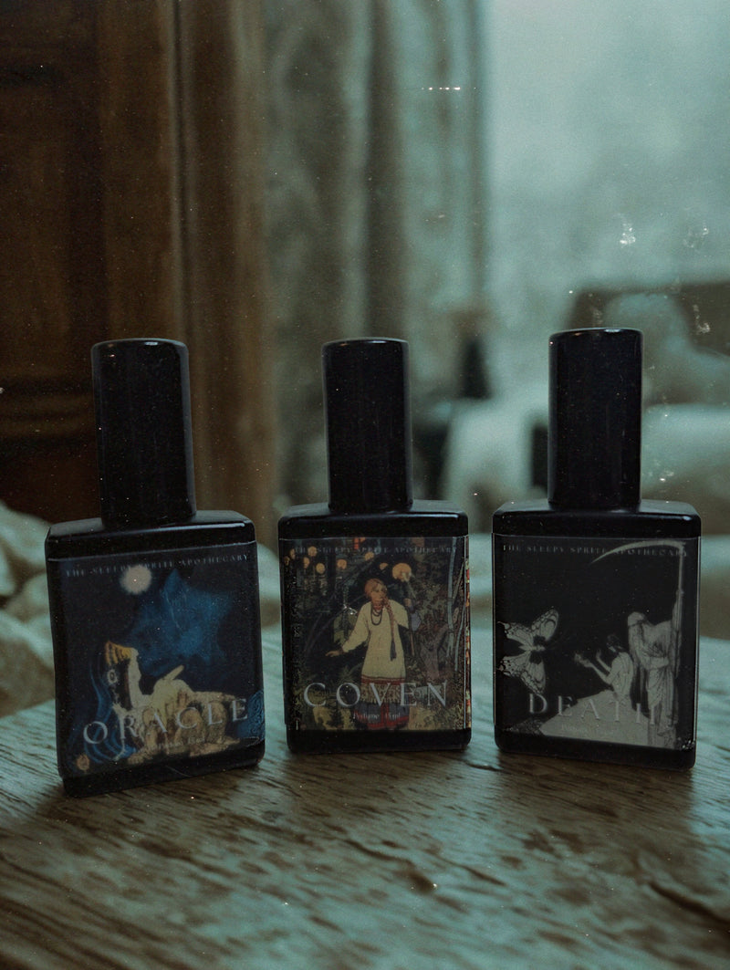 Three black perfume bottles with decorative labels on a wooden surface. Lore and Occult inspired perfumes.